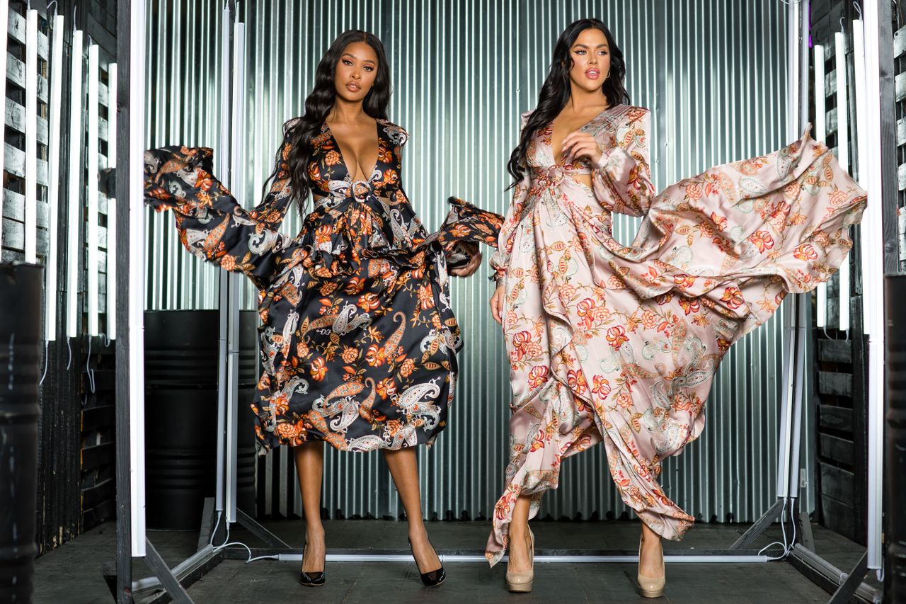 about-us-01 Two models in stylish patterned dresses posing in a studio environment.